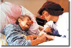 Foto einer Klinik-Clown-Betreuerin am Krankenhausbett einer Seniorin