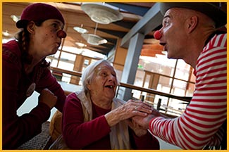 Foto von zwei KlinkClowns bei einer älteren Dame, die sie sich sehr über die Clowns freut